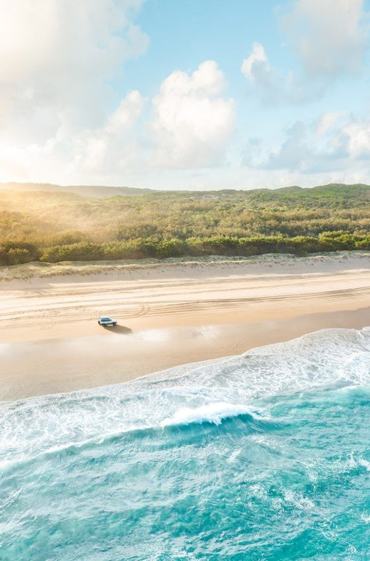 Vue aérienne d'une plage de Stradbroke Island avec un 4x4 roulant sur le sable, entourée d'eau turquoise et de végétation luxuriante