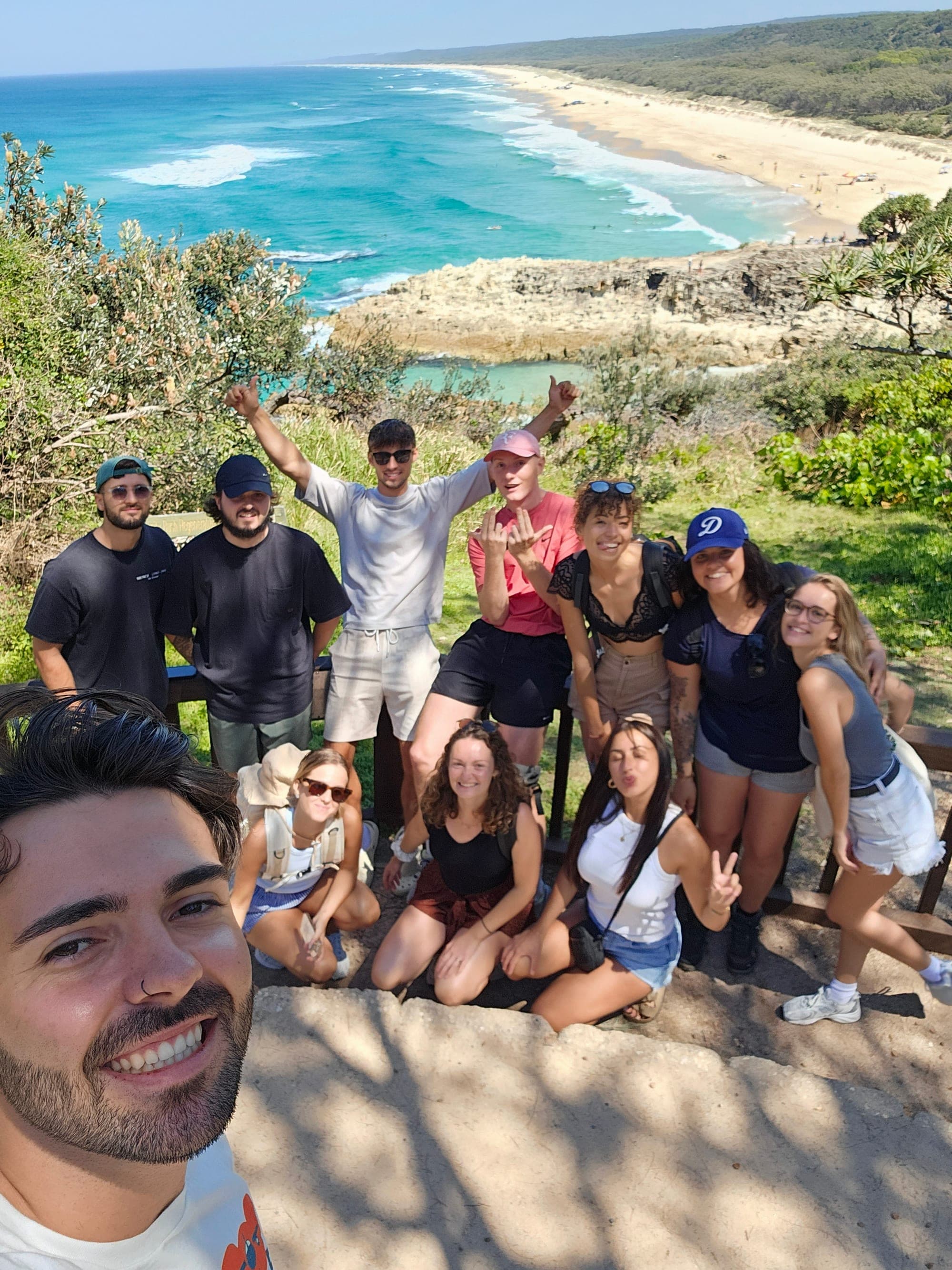 Tour group selfie at a coastal lookout above a long sandy beach on Minjerribah