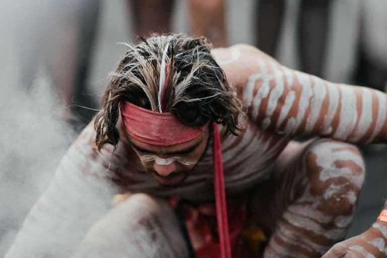 An Aboriginal man participates in a smoking ceremony, surrounded by cleansing smoke, with hands covering her face in a moment of reflection. A sacred ritual in Indigenous Australian culture, often performed to welcome visitors and protect Country.