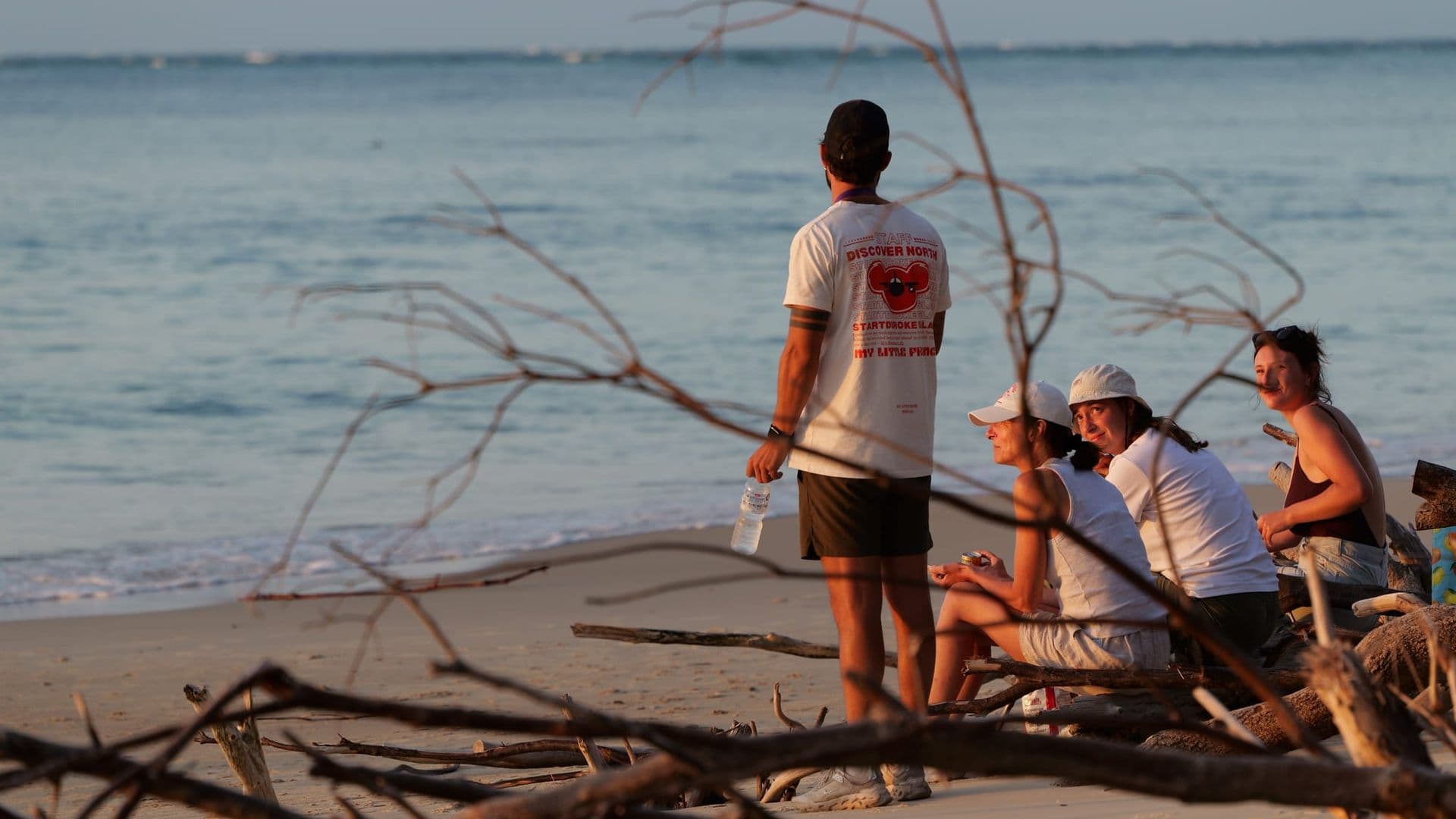 Tour group watching the sunset on a North Stradbroke Island beach amid driftwood