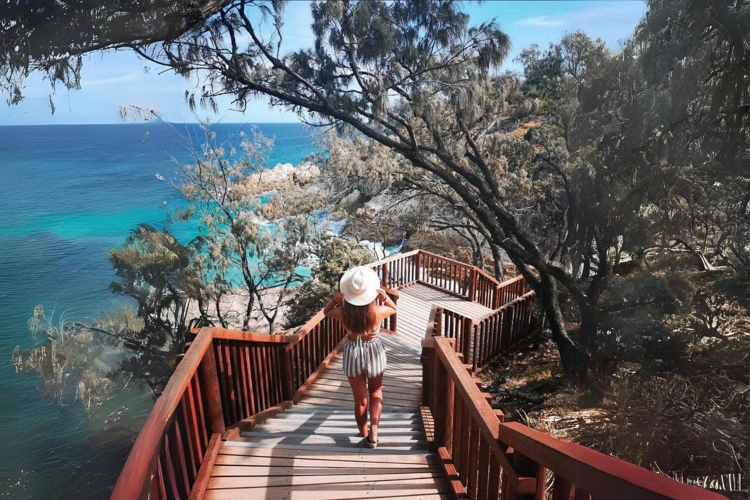 Person walking the timber boardwalk of the North Gorge Walk above turquoise ocean, North Stradbroke Island
